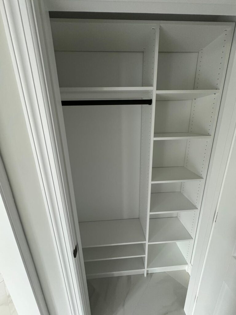 Empty reach-in closet with basic white shelving system and hanging rod for simple storage