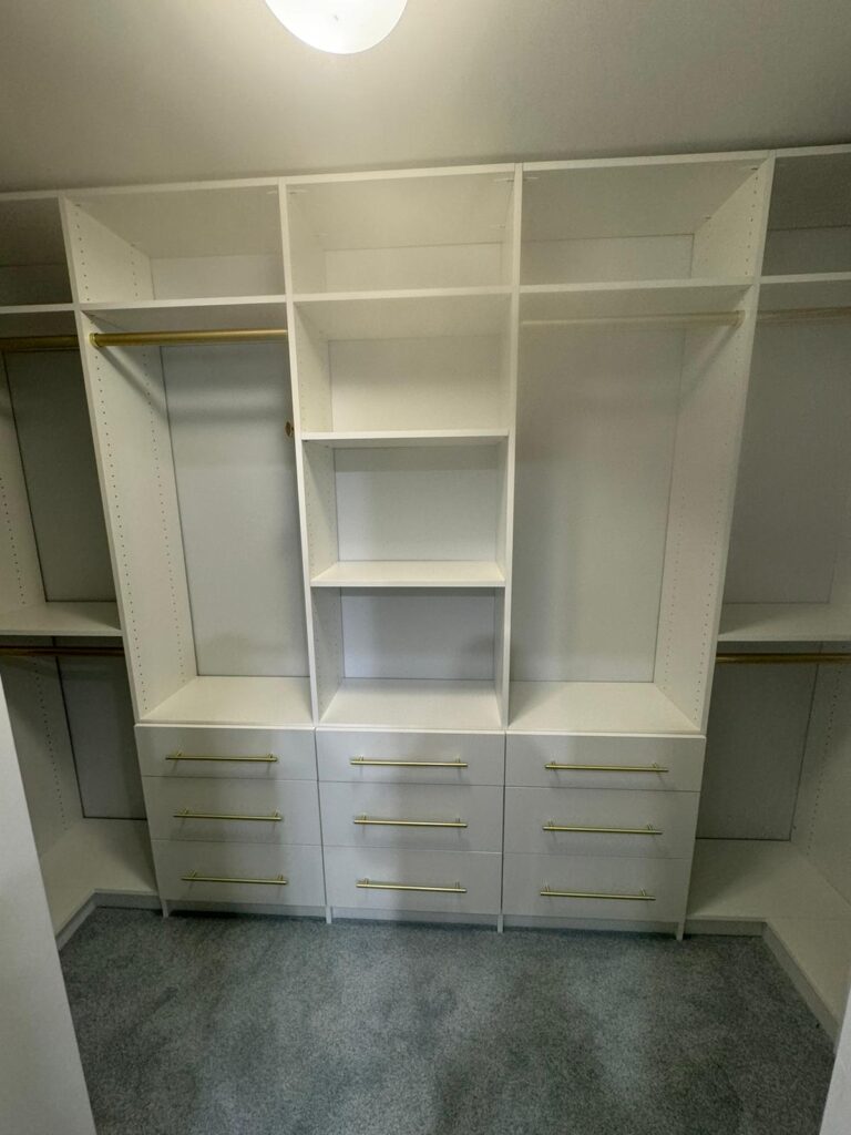 Empty walk-in closet featuring white systems with gold hardware accents and elegant finish details