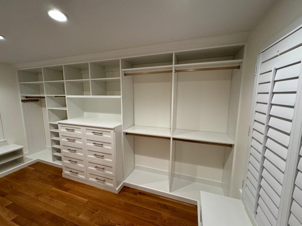 Empty walk-in closet with white organizational system featuring central drawer unit and surrounding shelving