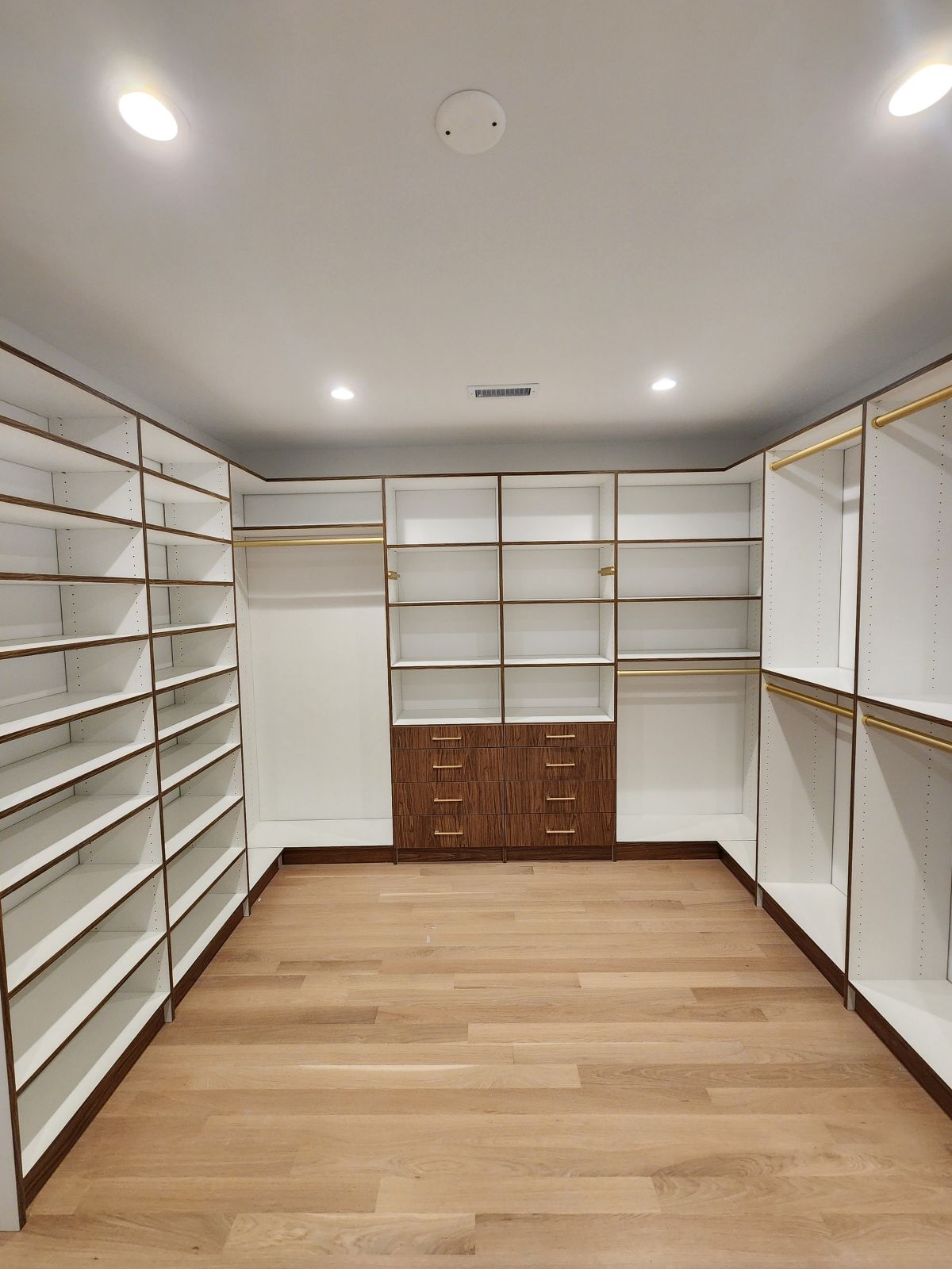 Empty walk-in closet featuring wood-grain accent drawers and white shelving systems