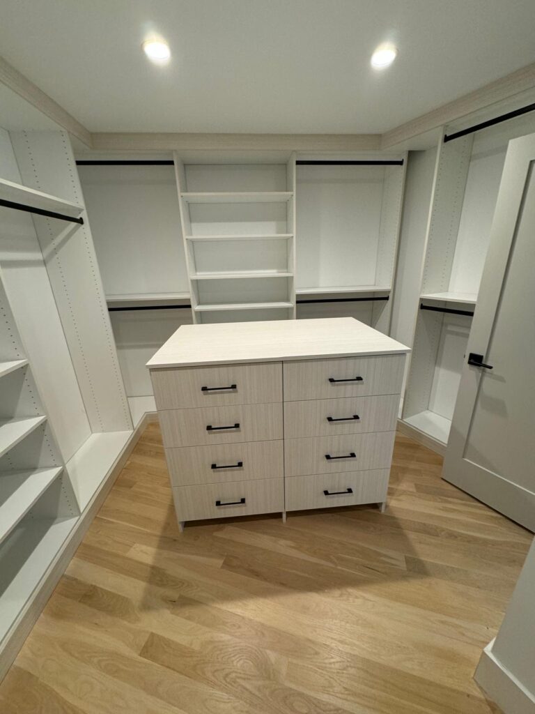 Empty walk-in closet featuring wood-tone center island with white surrounding storage systems