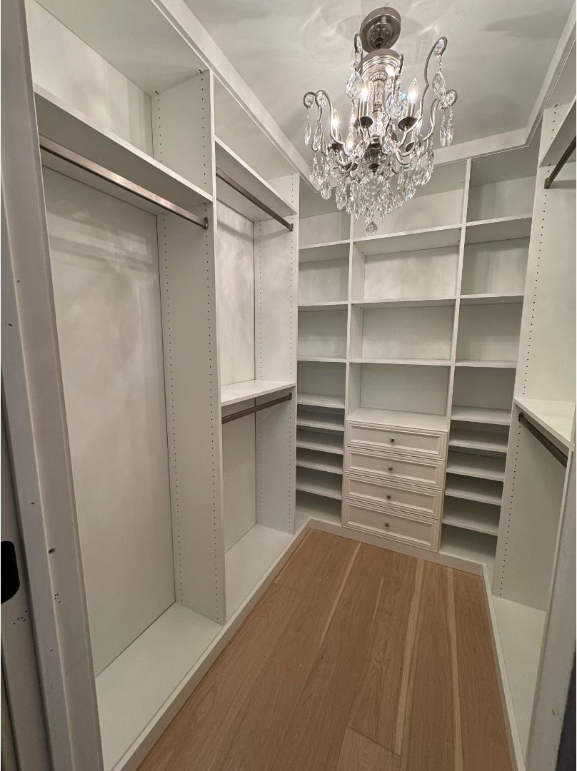 Luxury walk-in closet with crystal chandelier, white built-in storage, and premium finishes