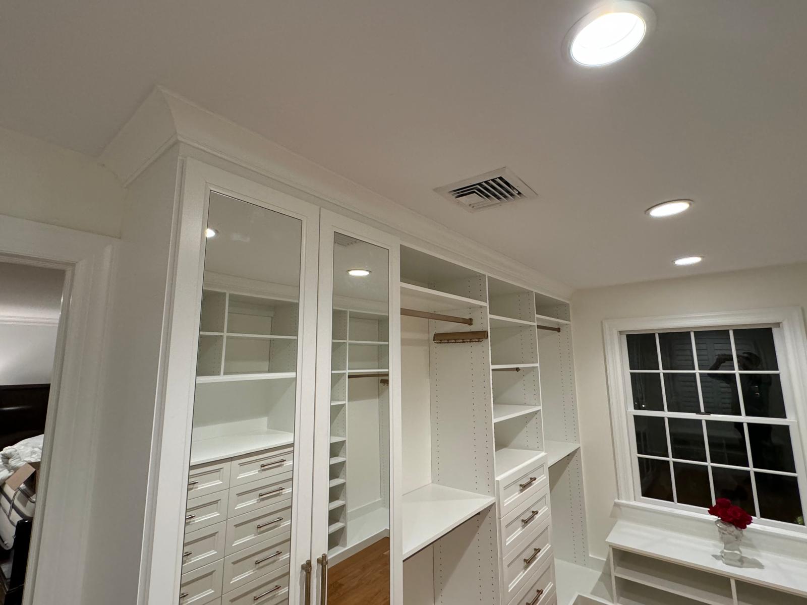 Luxury walk-in closet with glass-front cabinets, mirrors, and premium white storage systems