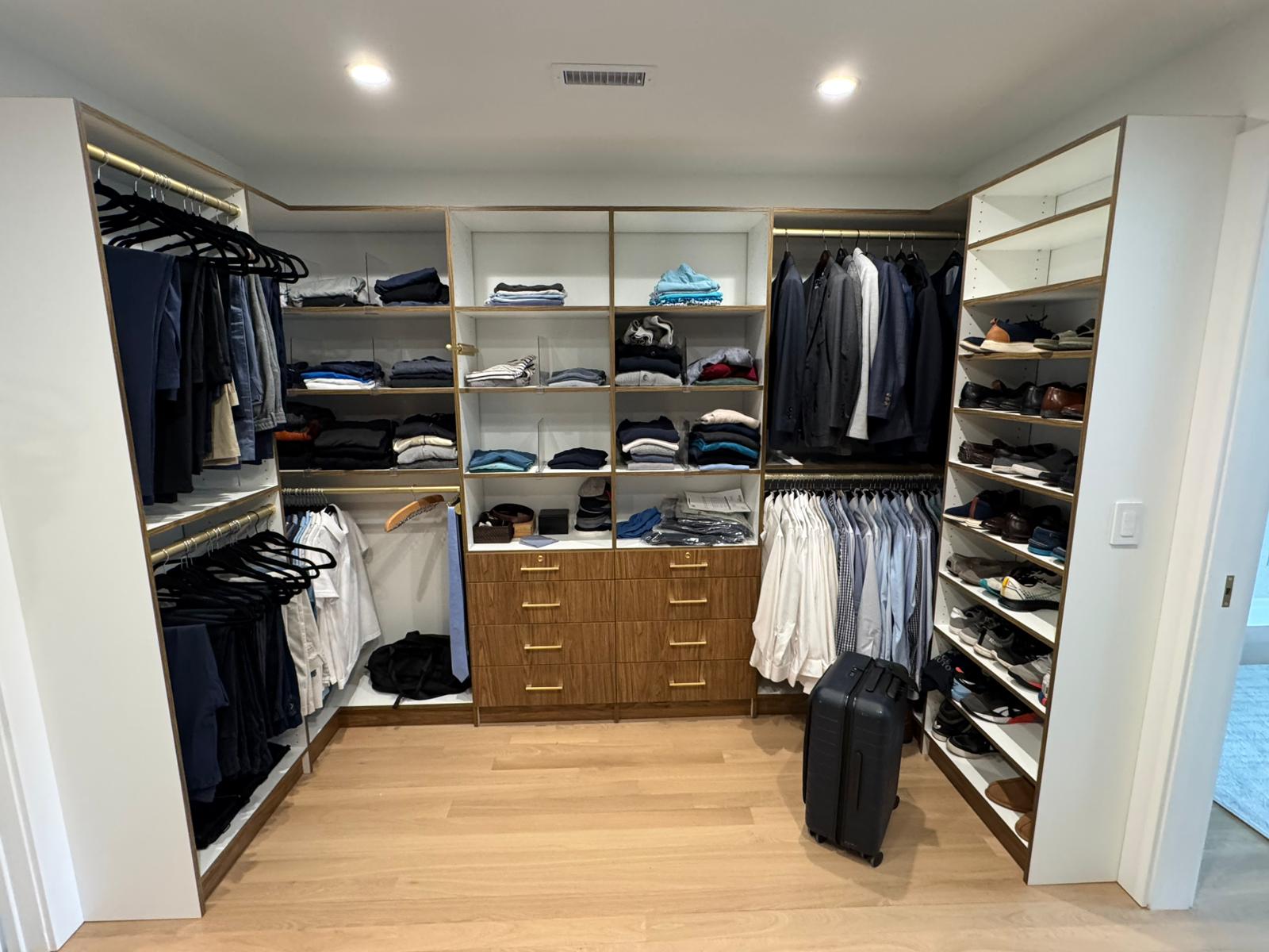 Men's walk-in closet with wood accent center tower, fully stocked with clothing and accessories