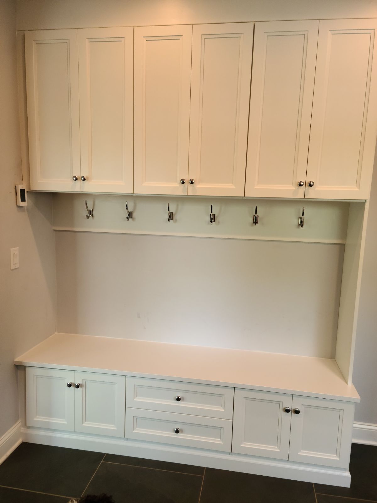 Mudroom with white storage bench, upper cabinets, and coat hooks for entryway organization