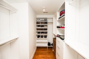 Narrow walk-in closet with white melamine shelving, central shoe storage, and drawer units