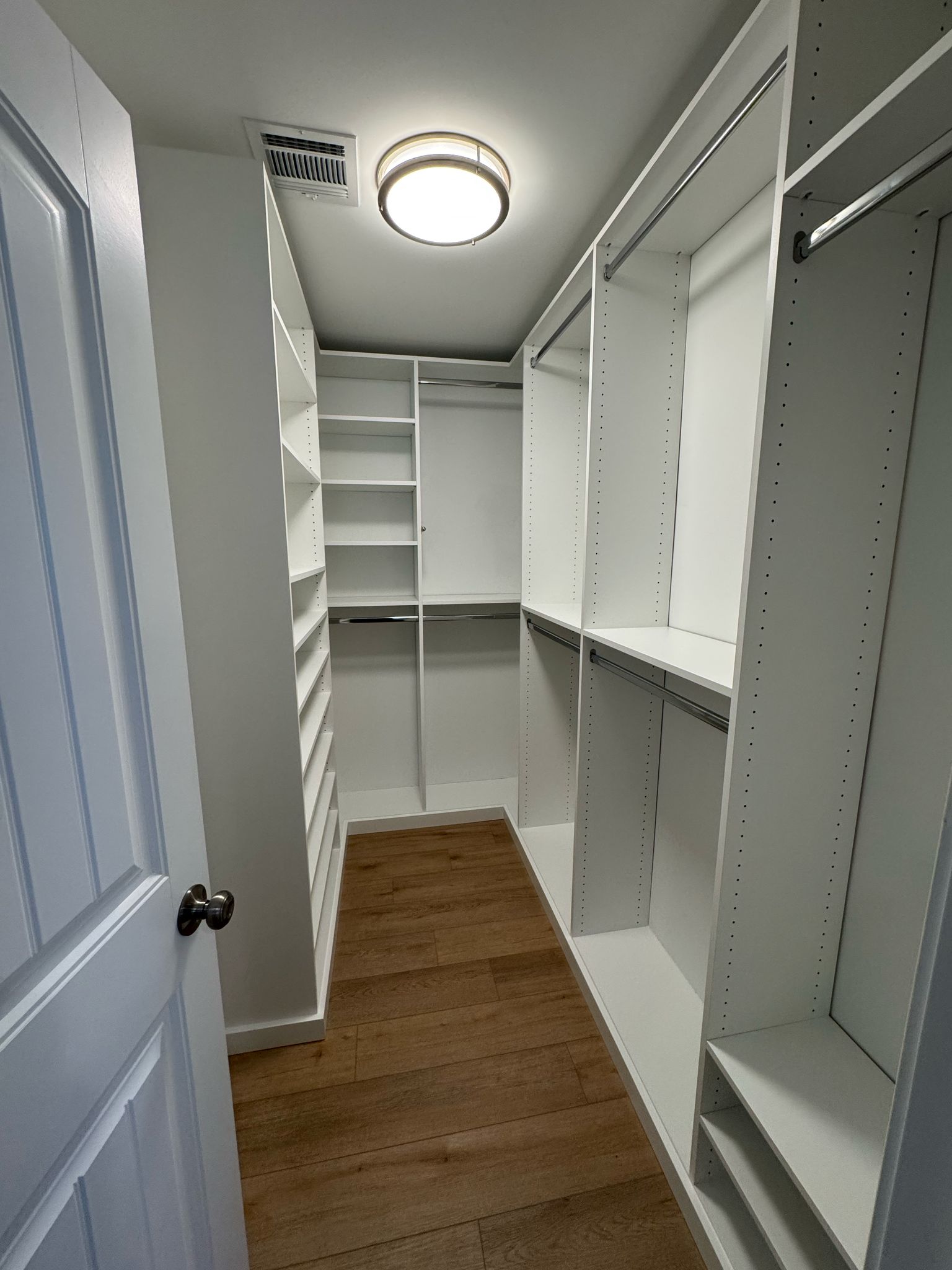 Small empty corner walk-in closet with white shelving systems and corner optimization design