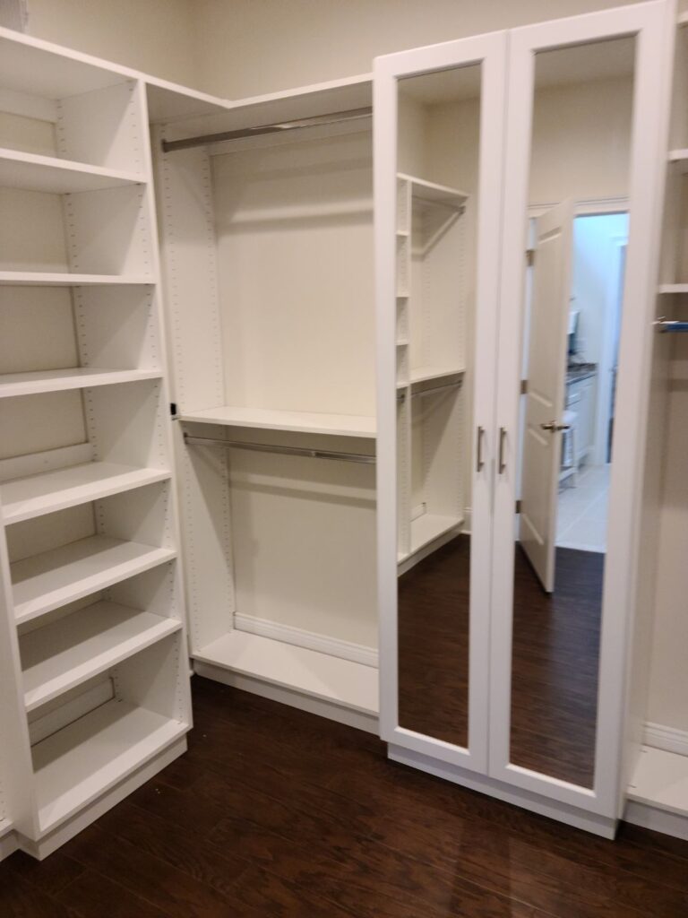 Walk-in closet featuring full-height white storage systems and mirrored doors