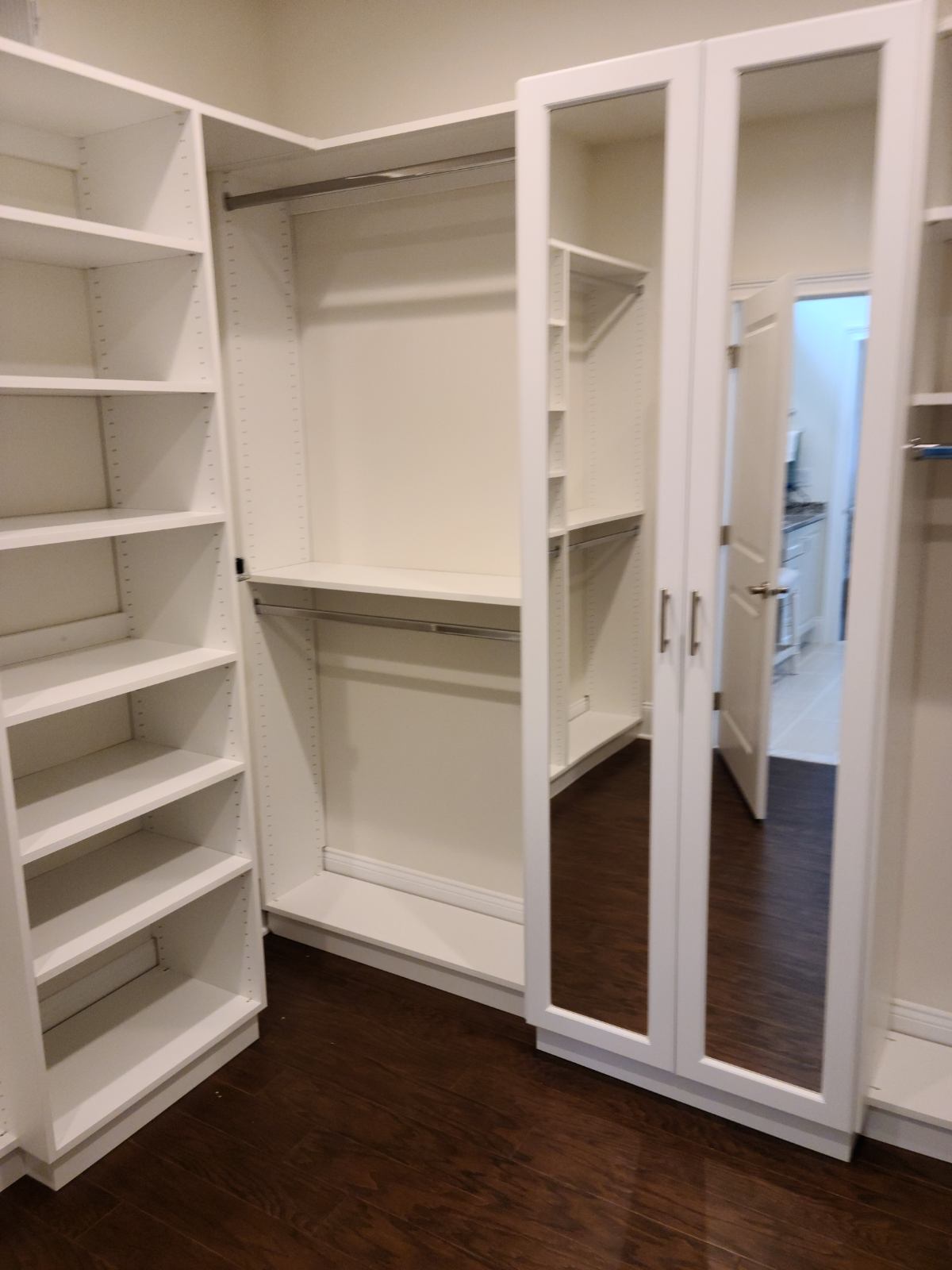 Walk-in closet featuring full-height white storage systems and mirrored doors