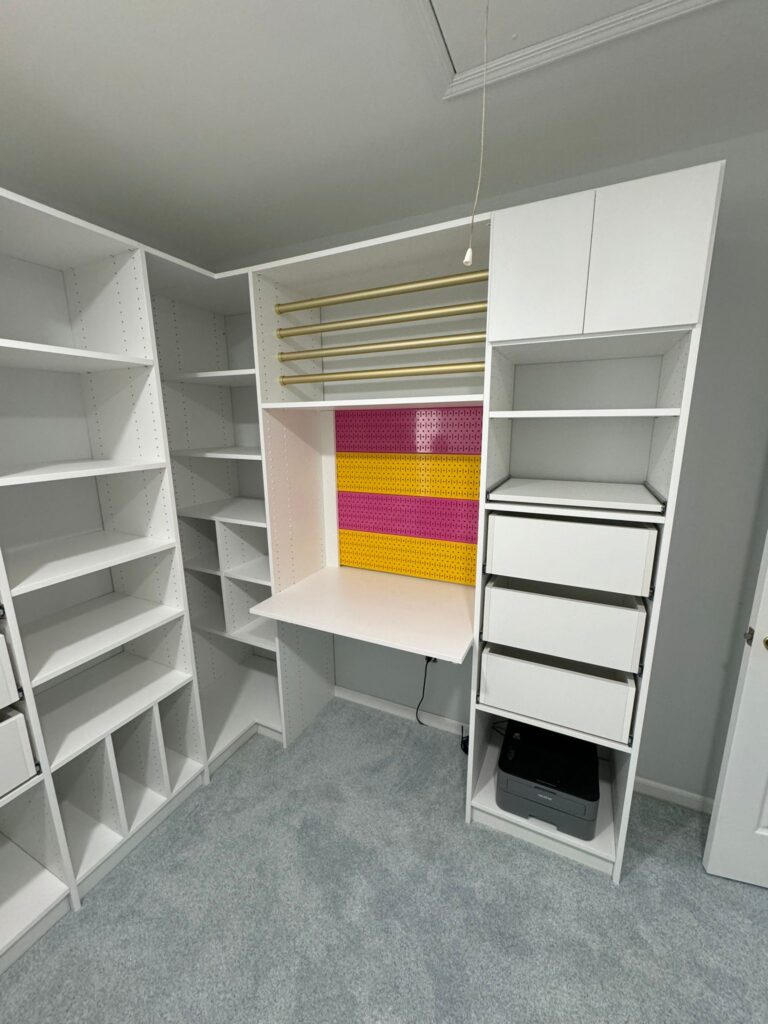 Walk-in closet with white systems, built-in workspace/vanity area with colorful accent panels