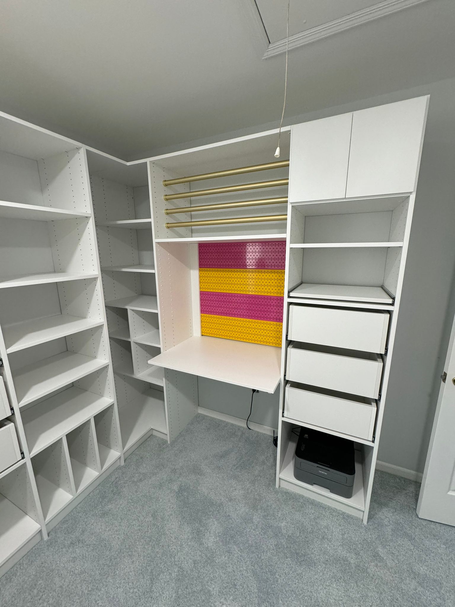 Walk-in closet with white systems, built-in workspace/vanity area with colorful accent panels