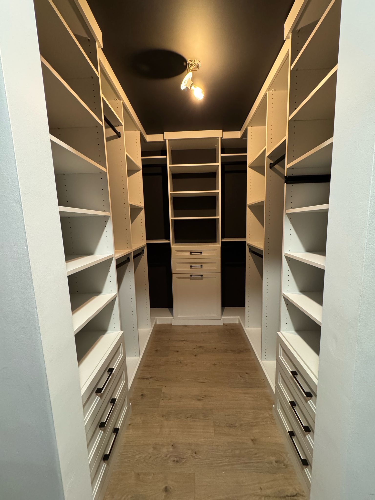 Walk-in closet with white shelving, double hanging sections, and central drawer tower