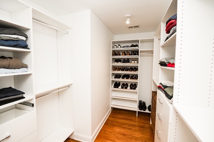 Walk-in closet showcasing extensive white shoe storage systems and hanging rod organization